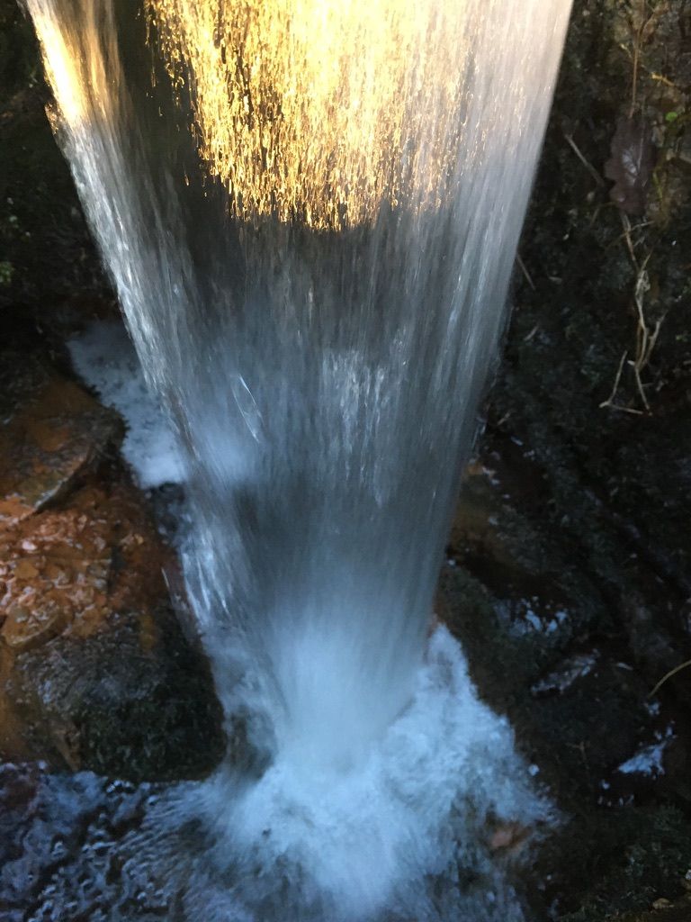 A column of water falling onto dark stones, lit gold at the top
